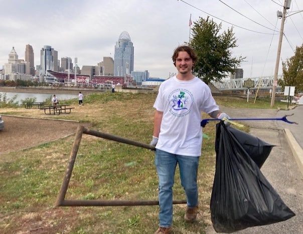 Environmental student carries metal debris, with Cincinnati skyline in background