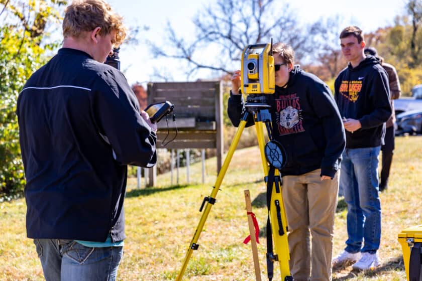survey students using a theodolite to measure horizontal and vertical angles outdoors