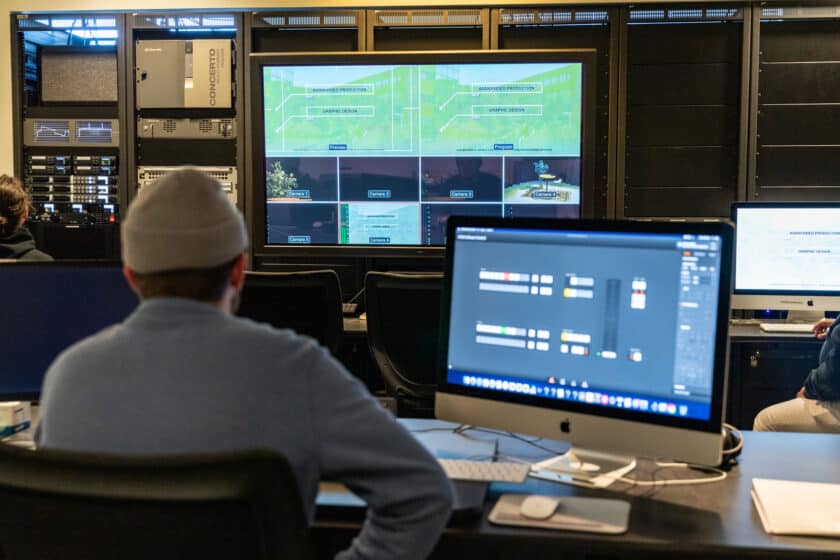 student at a computer in a audio/visual control room viewing monitors with multiple camera angles. 