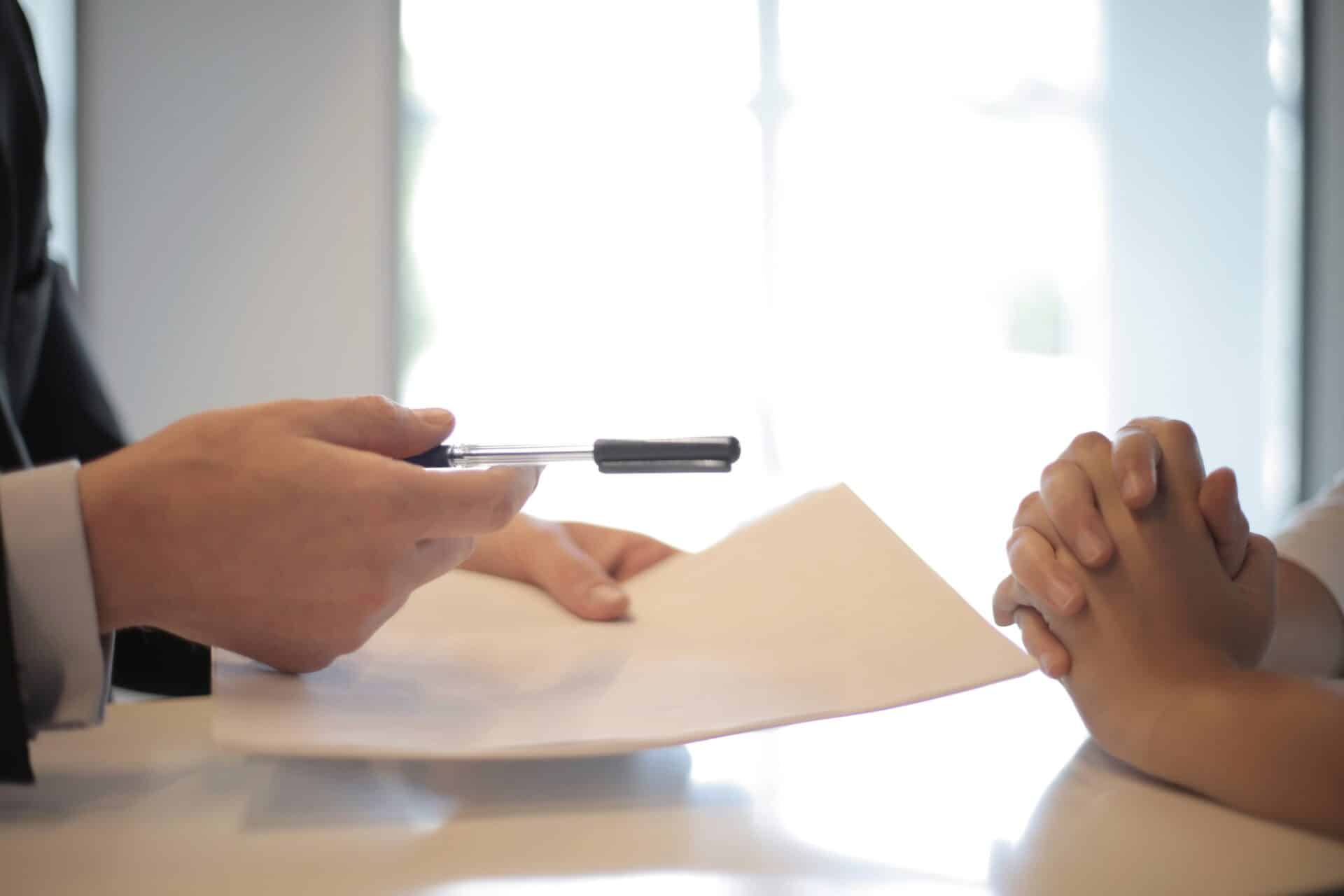 hands visible of two people sitting across from each other one person holding a pen and paper