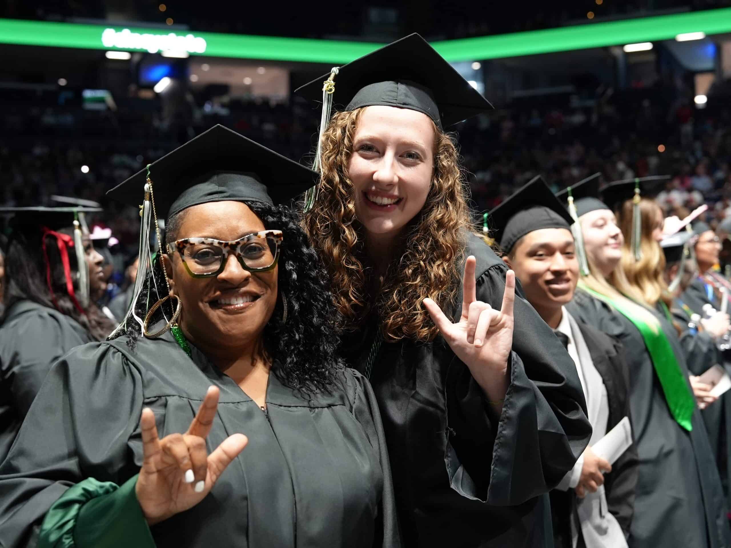 Two female graduates showing the ASL "I love you" sign
