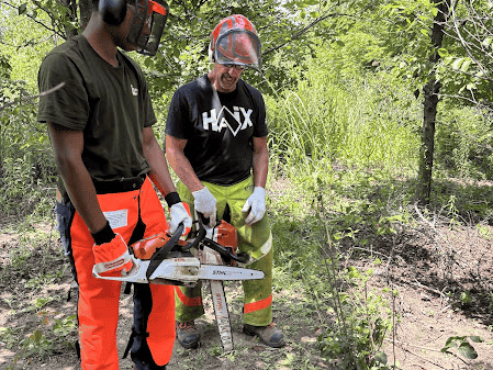 Two people outside working with chainsaws and protective equipment