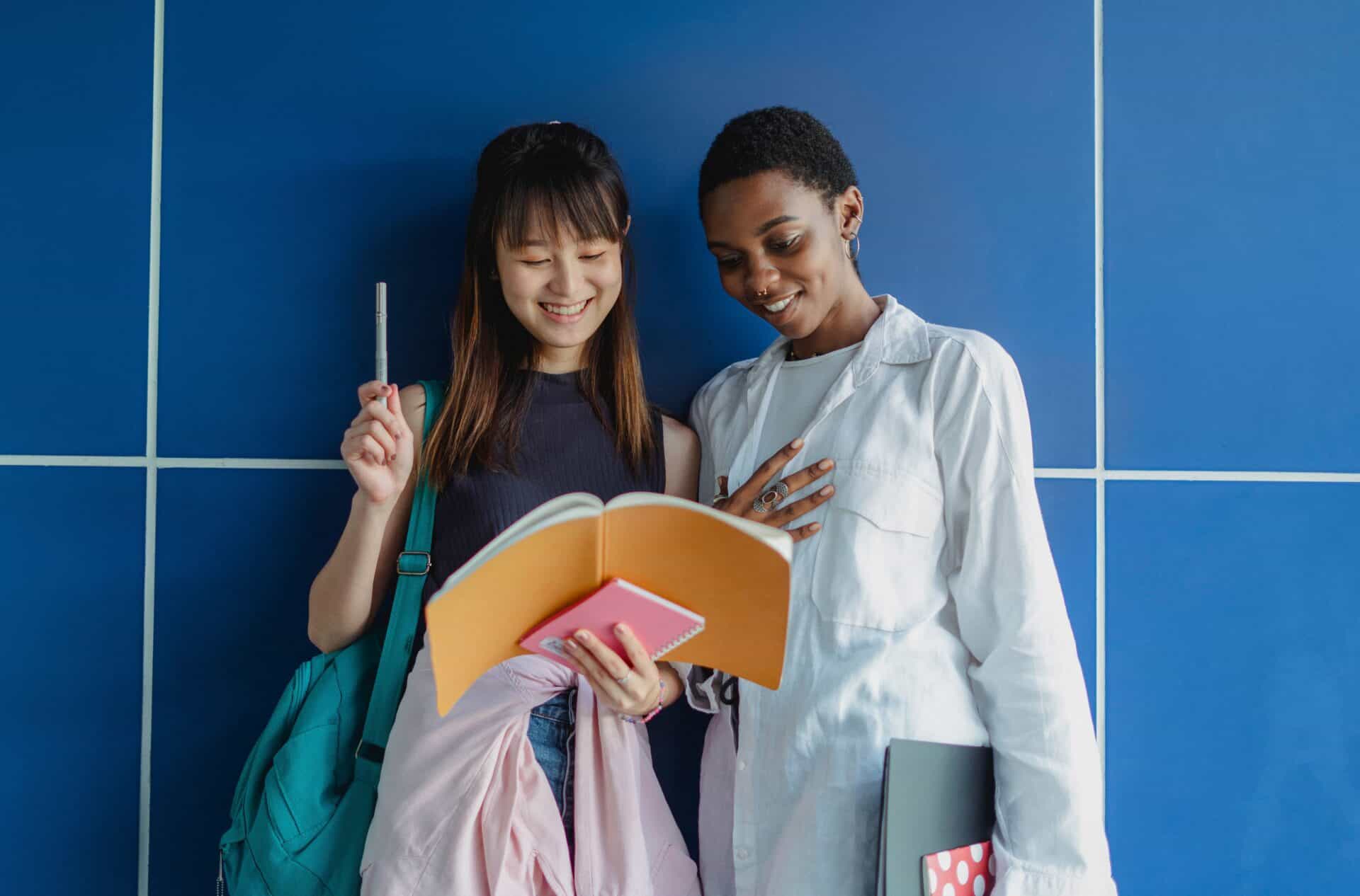 two students smiling at a notebook against a blue wall